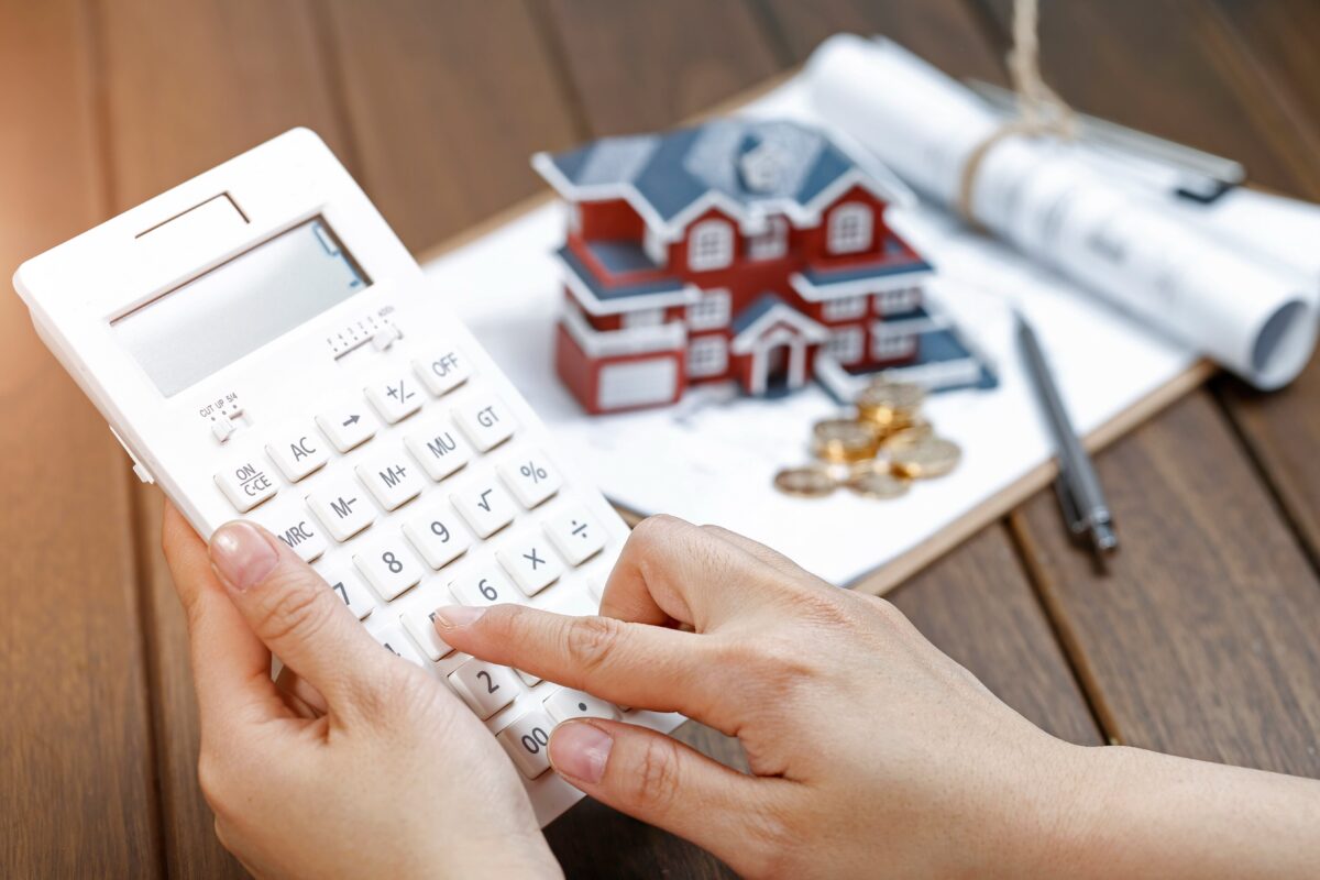a-female-hand-operating-a-calculator-in-front-of-a-villa-house-model-min